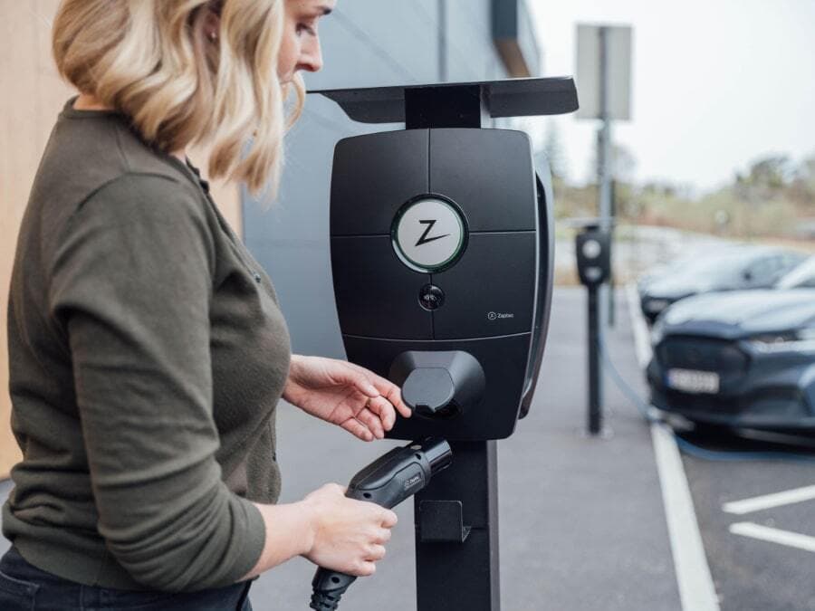 Frau, die an einer Ladestation von Zaptec ihr E-Auto Ladekabel einsteckt.