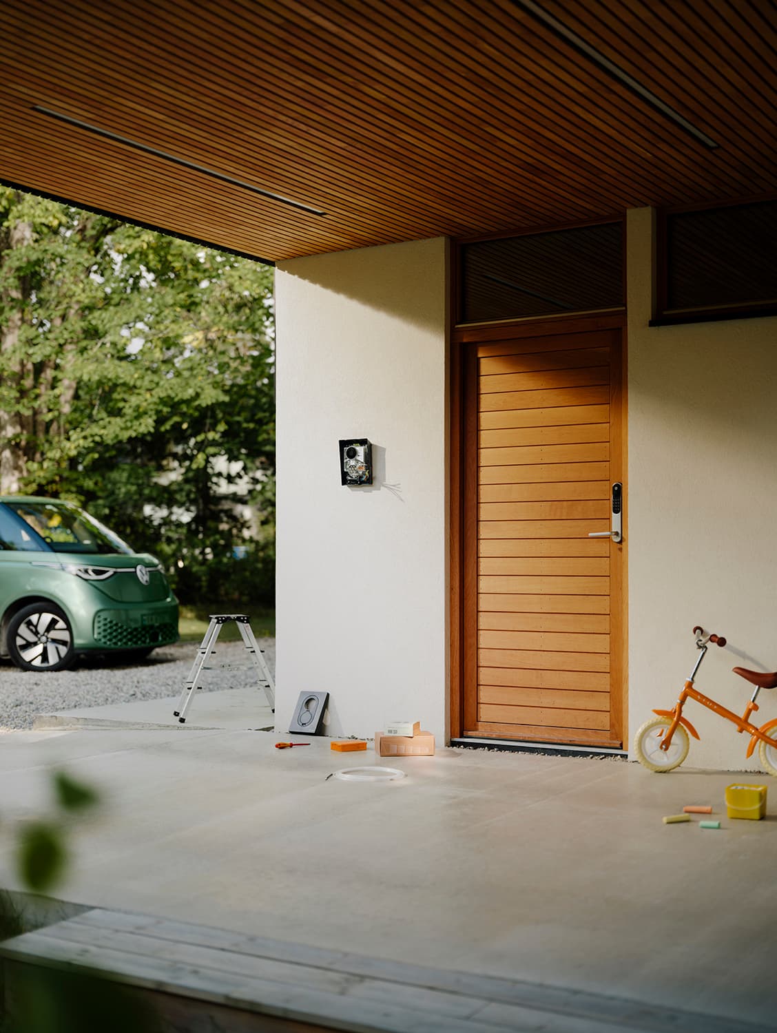 Uferdig Zaptec Go 2 hjemmelader på hvit vegg ved tredør, grønn varebil, verktøy og oransje barnesykkel utenfor.