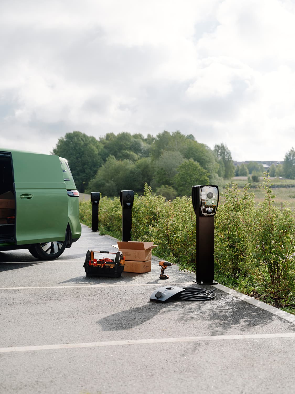 Zaptec Pro chargers mounted on columns in parking lot, green van, tools, and boxes in foreground, installation in progress.