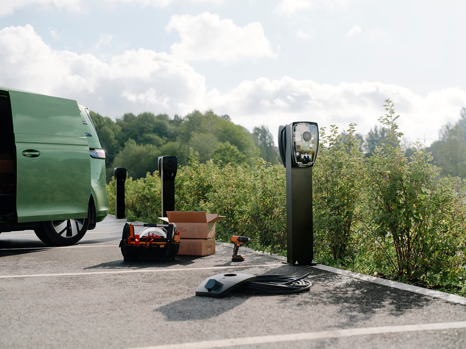 Zaptec Pro lader op kolom op parkeerplaats, groene bestelwagen, gereedschapskist, kartonnen doos en afdekking op de grond, installatiescène.