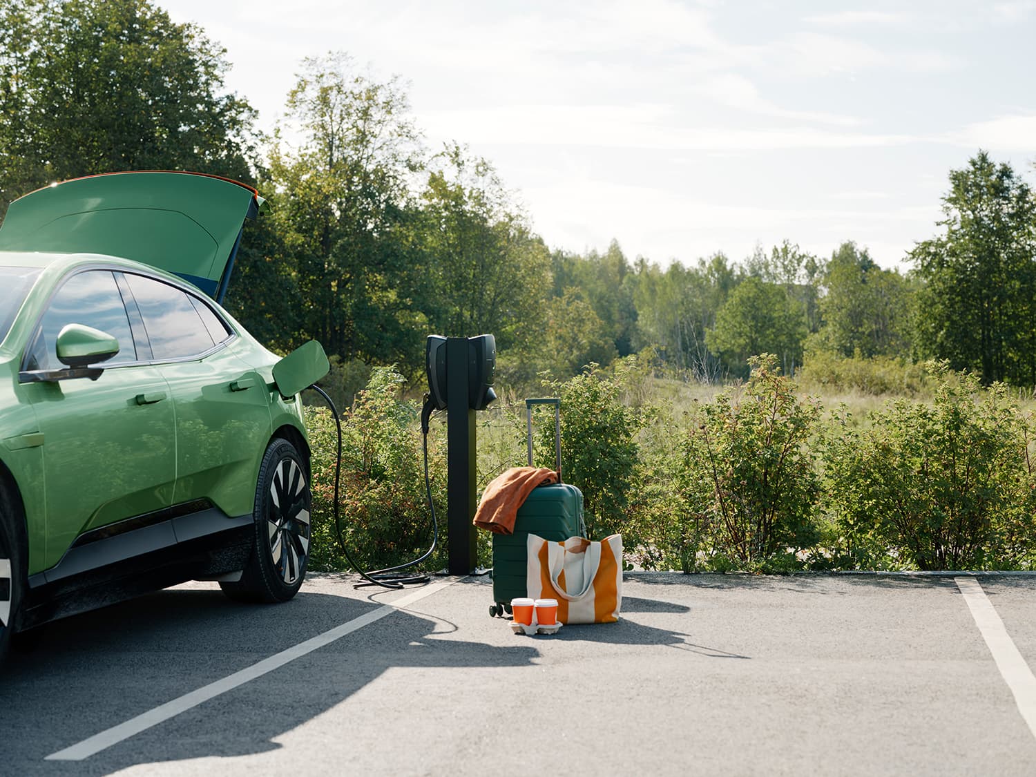 Groene auto laadt op bij Zaptec Pro lader op kolom op parkeerplaats, koffer, tas en bekers op de grond, open kofferbak.