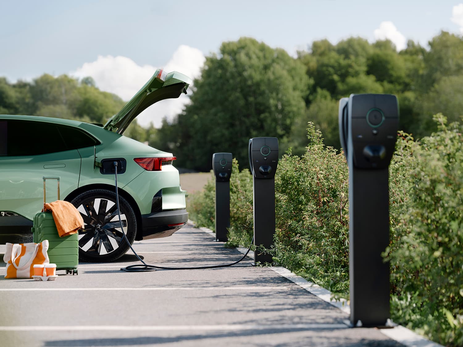 Green car charging at Zaptec Pro charger mounted on column, three chargers visible, suitcase and bag on ground, open trunk.