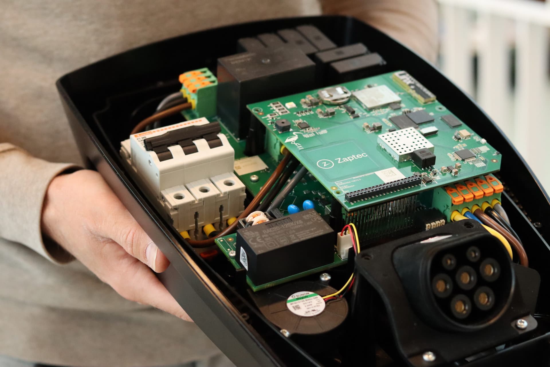 En person holder en åpen Zaptec-lader der de interne elektroniske komponentene er tydelig synlige.