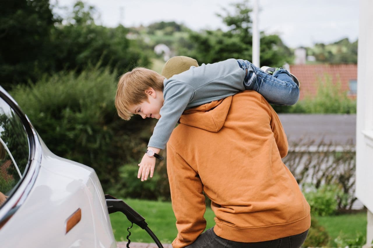Ein Kind und ein Mann laden ein E-Auto über ein Verlängerungskabel