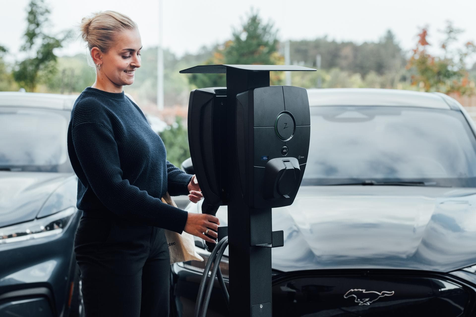 Eine Frau steht vor einer Wallbox auf einem Mehrfamilienhaus-Parkplatz