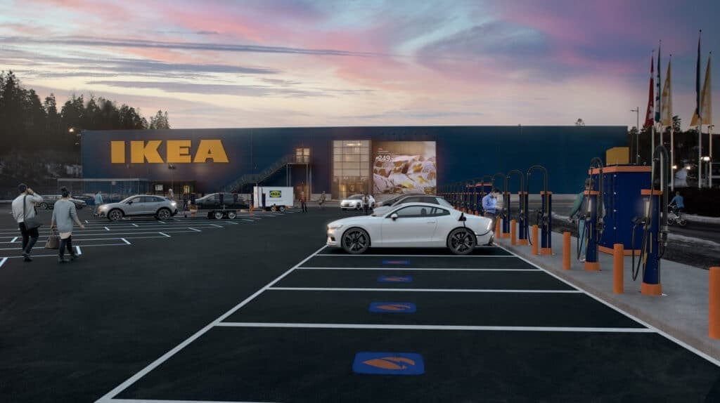 En hvit elbil lader utenfor en IKEA-butikk ved solnedgang. Flere ladestasjoner er plassert langs parkeringsplassen, og folk går mot inngangen til varehuset.