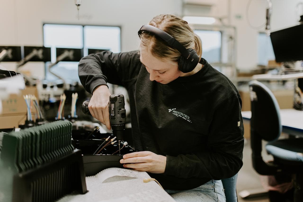 En person med hørselvern monterer komponenter i et fabrikkmonteringsmiljø med fokus og presisjon.