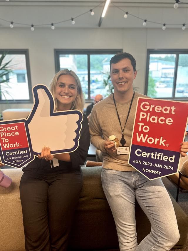 en kvinna i mörka kläder med ljust hor och en man i kort mörk frisyr och beiga kläder håller en varsin skyllt med budskap från Greta place to work